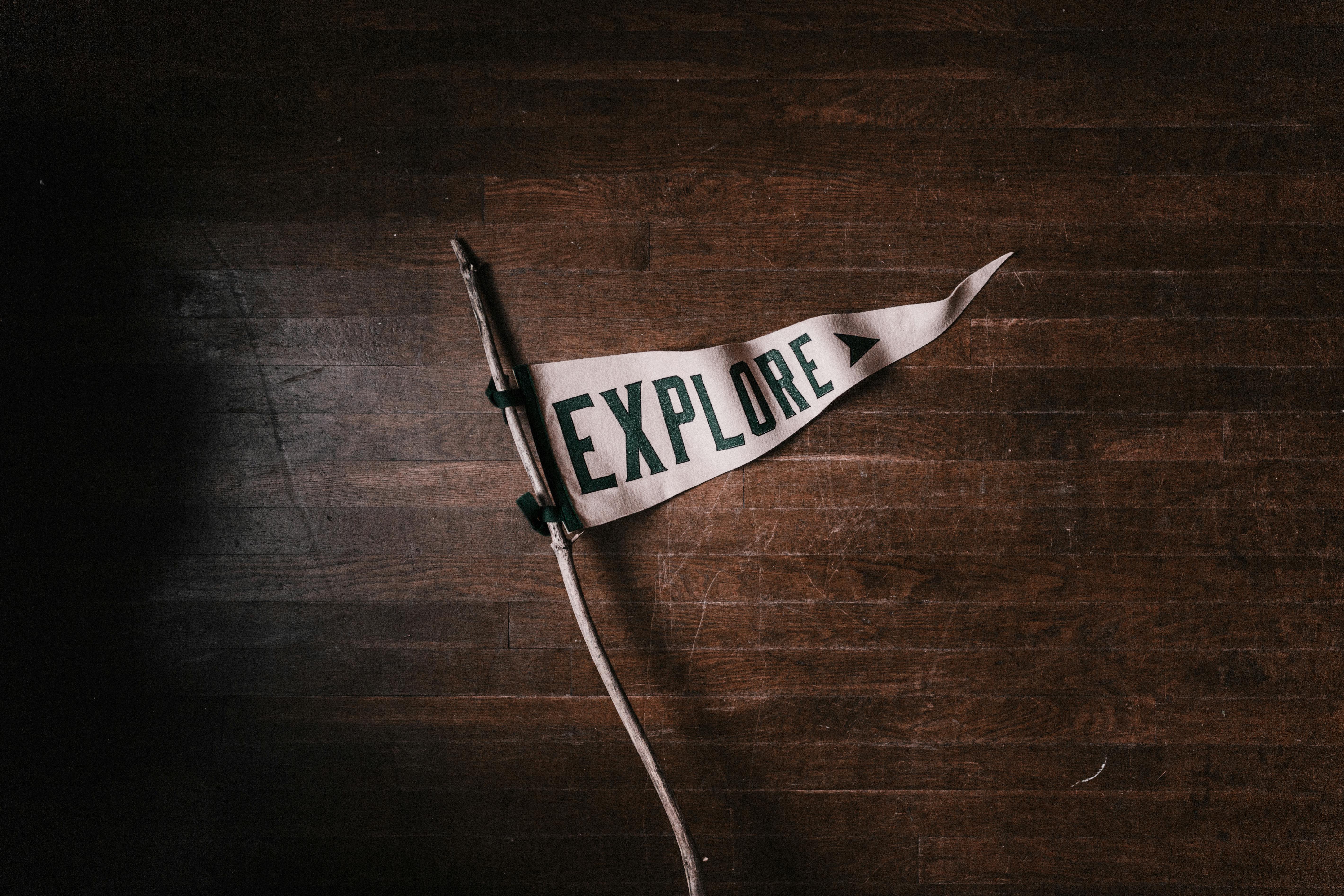 Artistic flat lay of an 'Explore' pennant on rustic wooden flooring, emphasizing adventure and exploration.