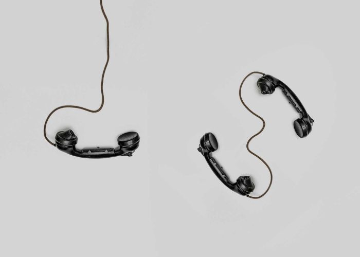 Two vintage black telephone handsets connected by cords on gray background.